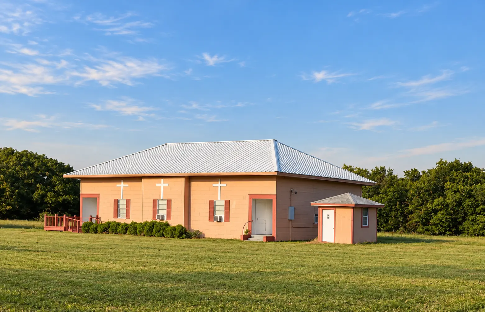 Allison Community Church: a peach-colored building with a white metal roof and three white crosses on its front wall, in a grass field.
